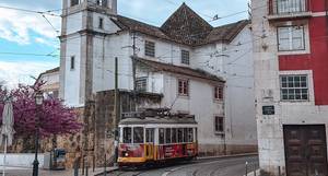 Lissabon - gelbe Tram in der Alfama mit historischer Kirche